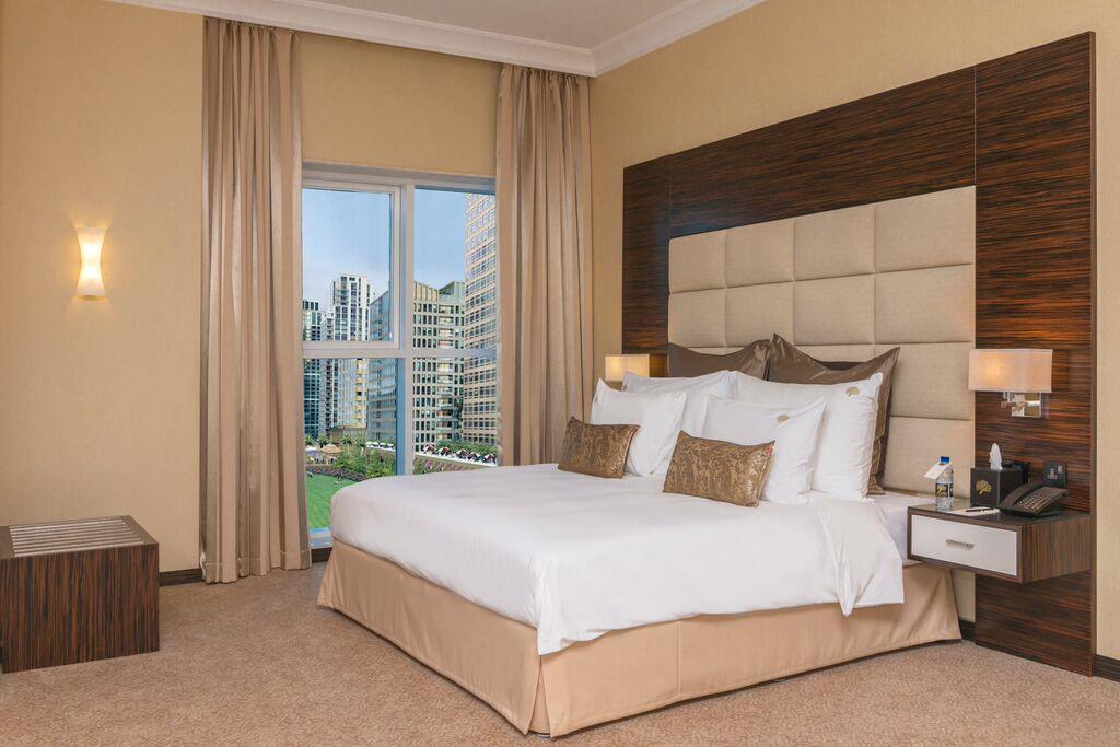Jannah Burj Al Sarab Hotel Abu Dhabi Buitenkant foto The photo shows a well-decorated hotel room featuring a large bed with white bedding and decorative pillows. The walls are painted in a warm color, and there are modern wooden accents. On one side, there are light fixtures, and beside the bed, there 